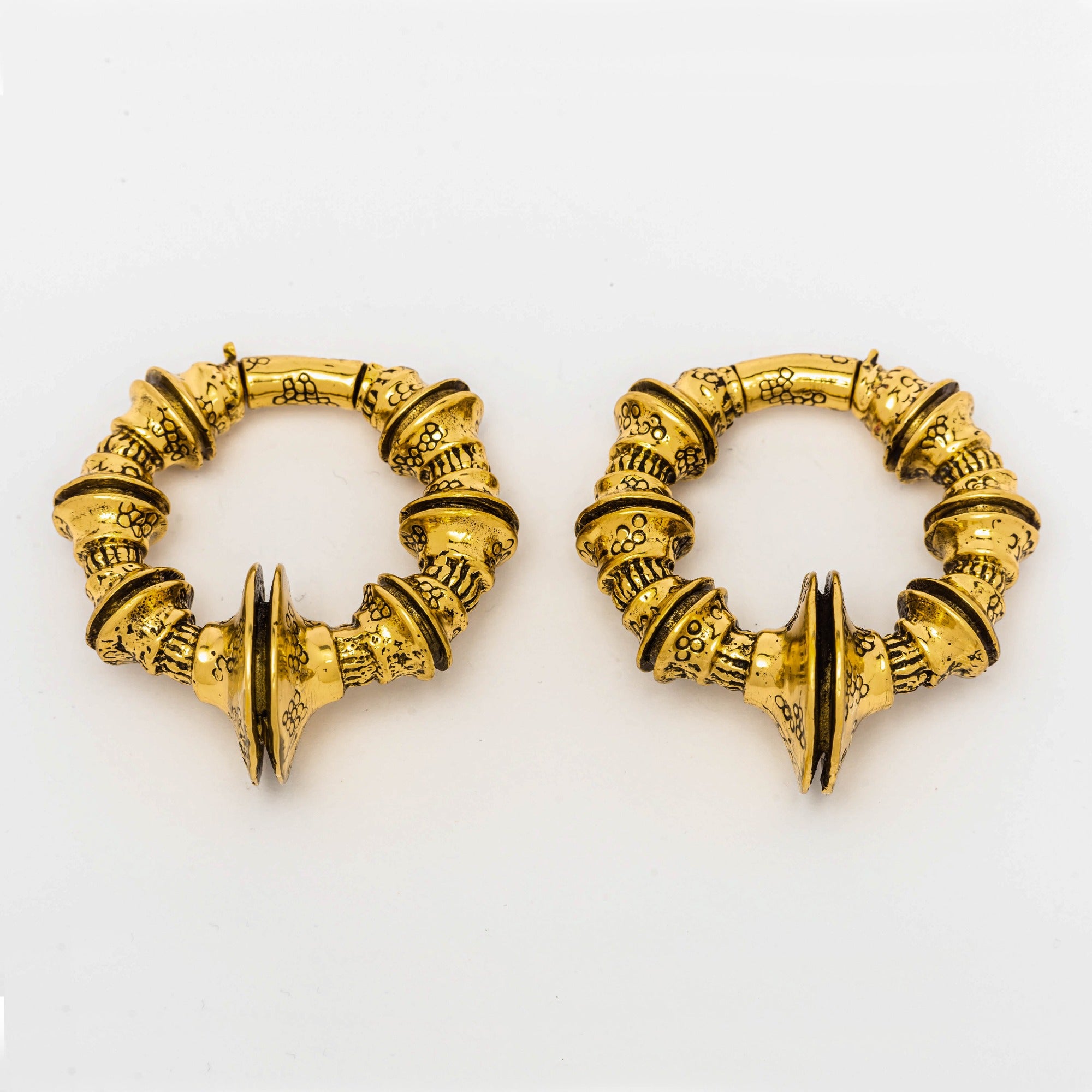 A pair of gold TRAKARA Heavy Tribal Cyborg Clicker Ear Weights from Kaya Movement, featuring a 2 gauge size. The ear weights showcase an intricate, round design with elaborate segmented patterns and textured detailing, creating a decorative and elegant appearance reminiscent of tribal cyborg aesthetics. Each piece includes a pointed, symmetrical decoration at the center.